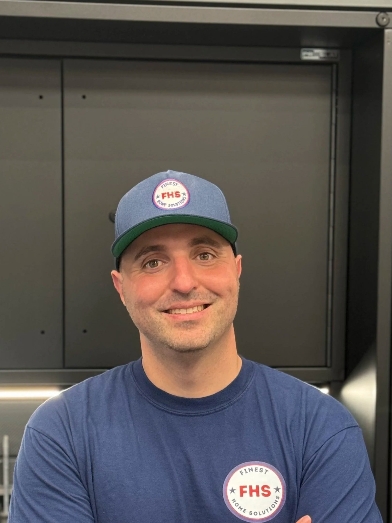 A smiling man with a shaved head and light skin, wearing a light-colored button-up shirt, looking at the camera against a white background.