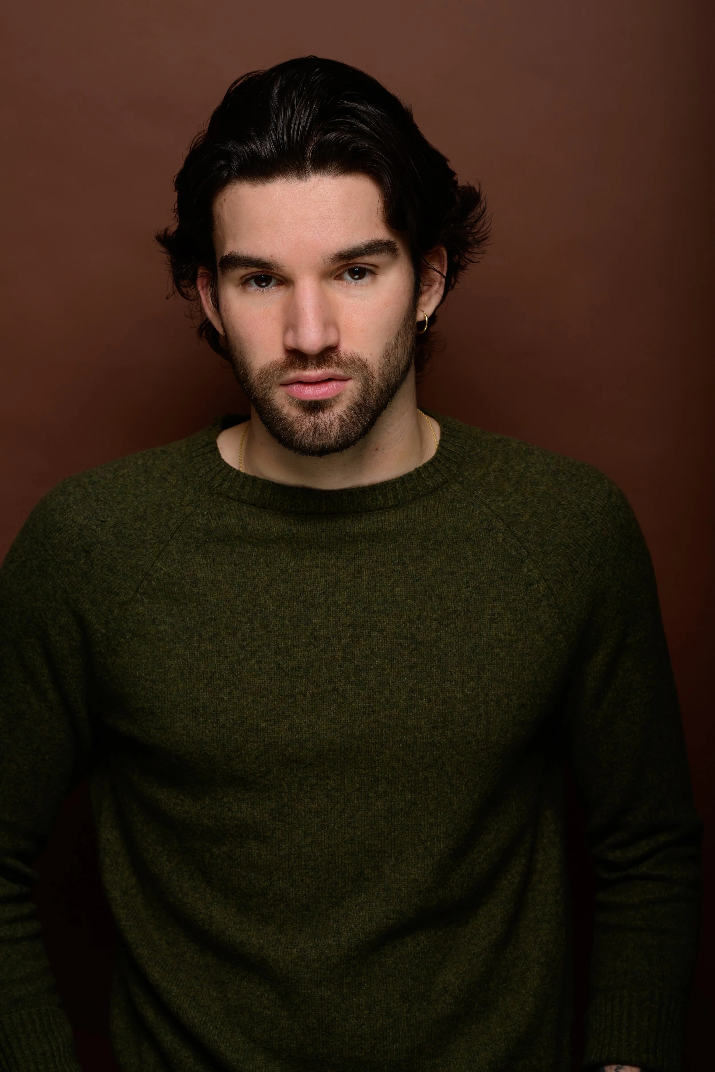 Luca with dark hair and a beard wearing a red sweater, standing against a white wall.