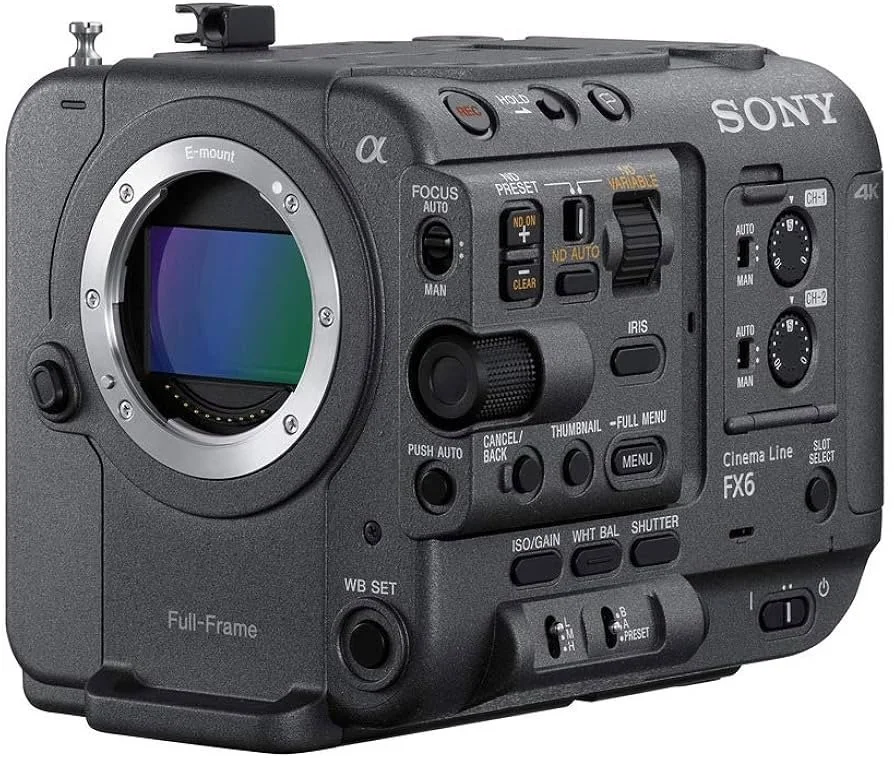 Close-up of a professional camera with a large lens, mounted on a stabilizer, held by a person’s hand against a dark background with blurred trees.