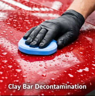 Hand in black glove using a blue sponge to decontaminate a red surface with water droplets, labeled 'Clay Bar Decontamination'.
