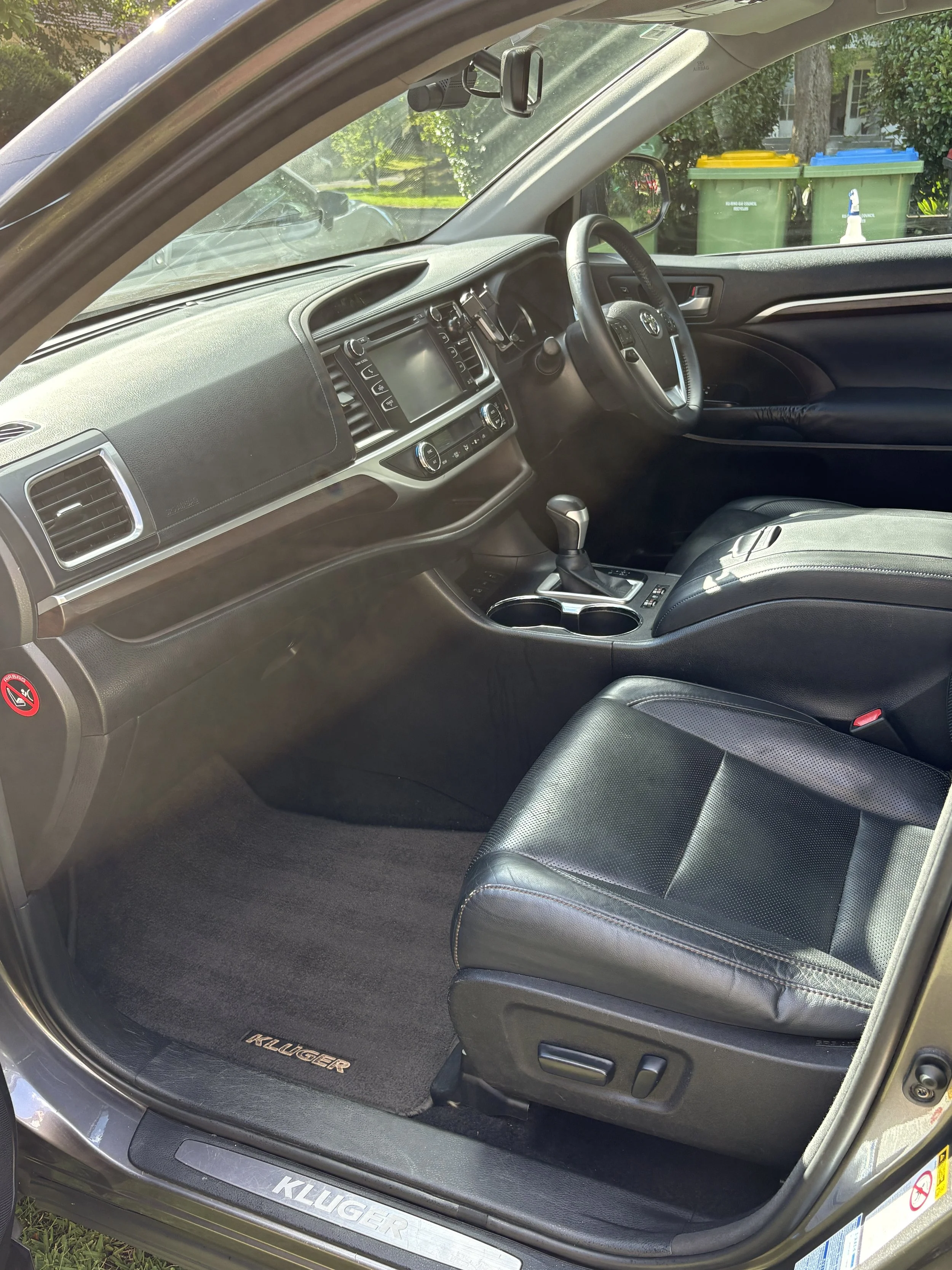 Interior of a Toyota Kluger, showing the driver's seat, dashboard, center console, and steering wheel with a gear shift and cup holders.