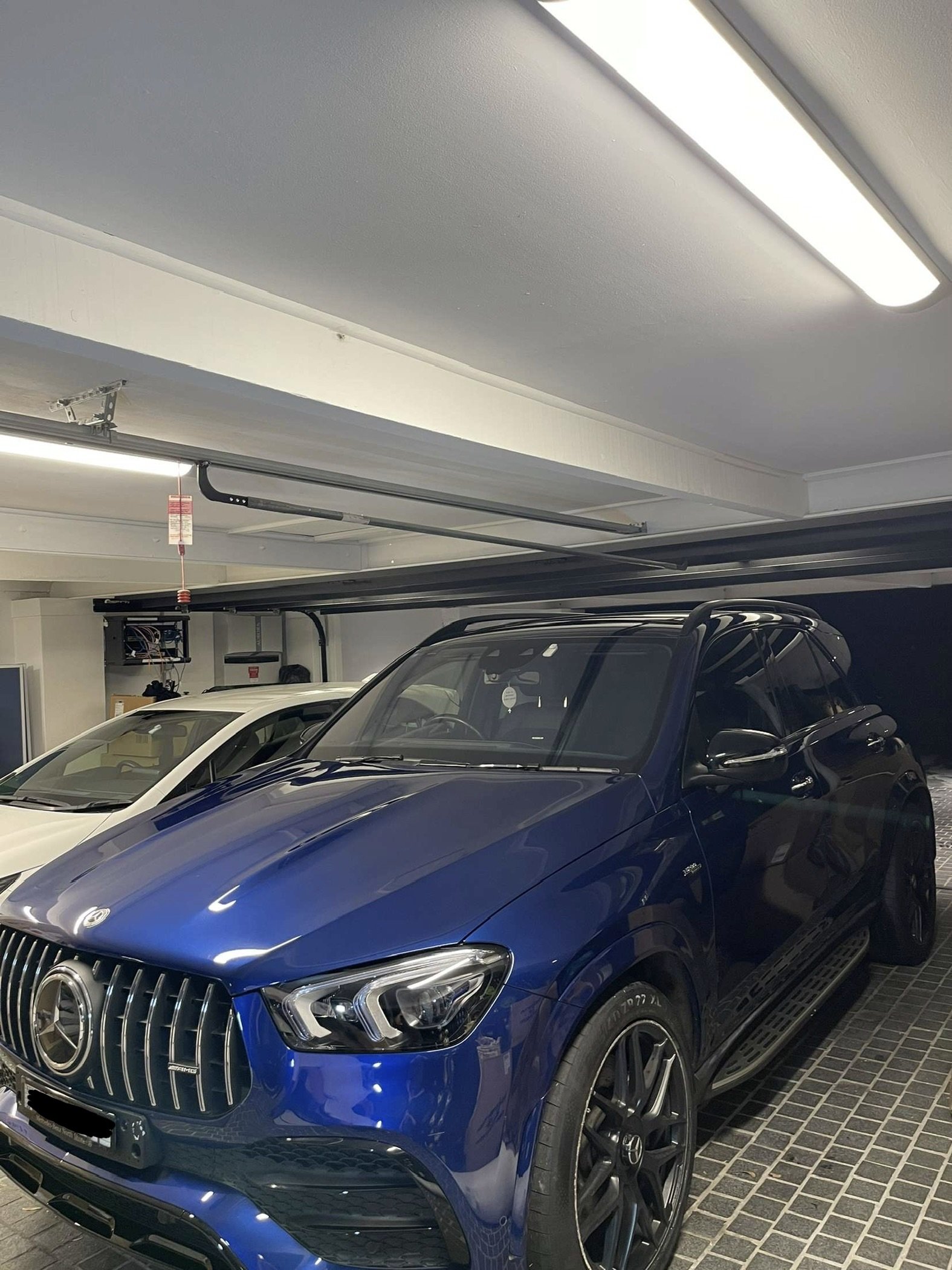 Blue Mercedes-Benz SUV parked in an indoor garage next to a white vehicle.