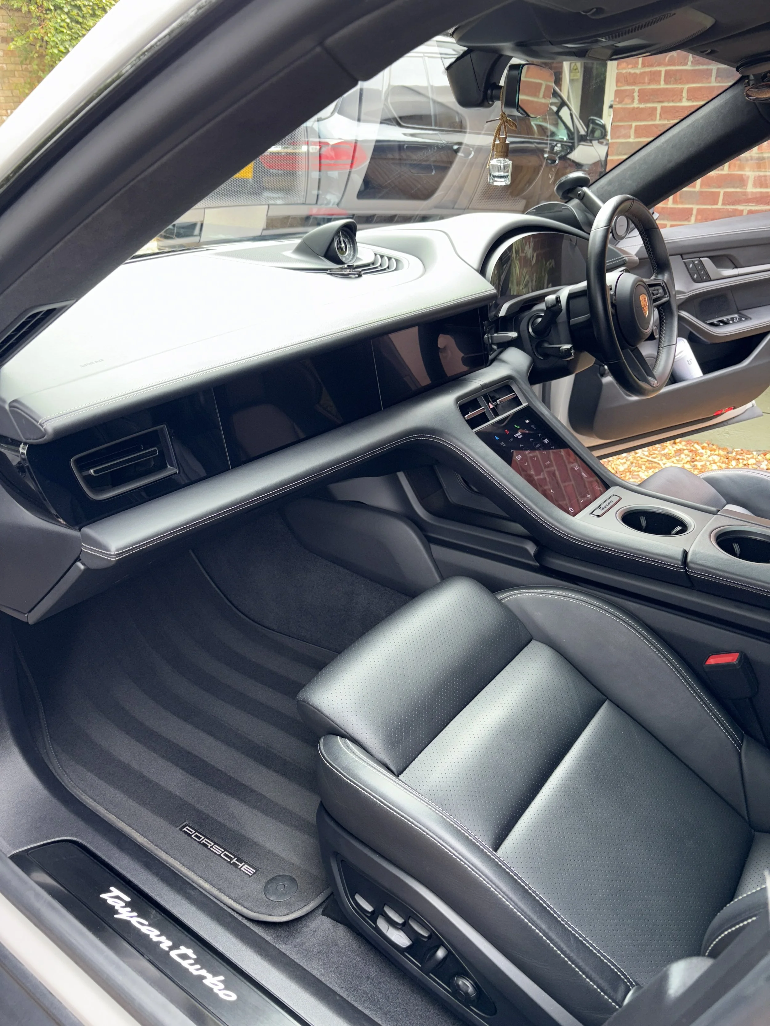 Interior of a Porsche Taycan Turbo electric car showing the dashboard, steering wheel, and passenger seat with black leather upholstery.