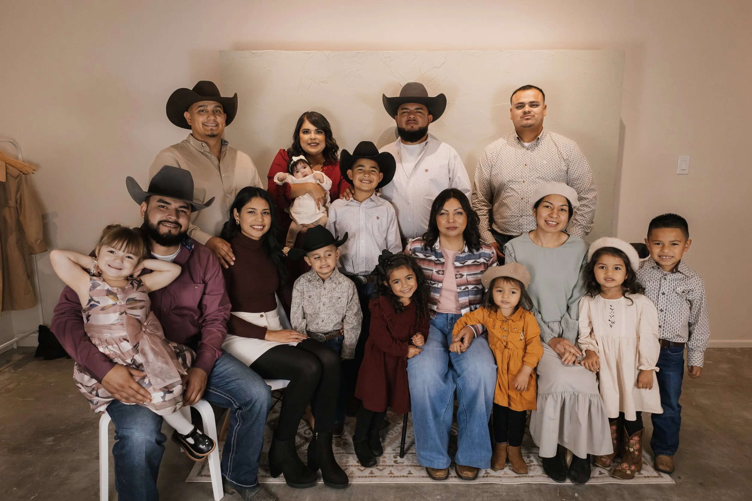 A large family group posing for a photo in a room, with some people wearing hats and casual attire, including children and adults of various ages.