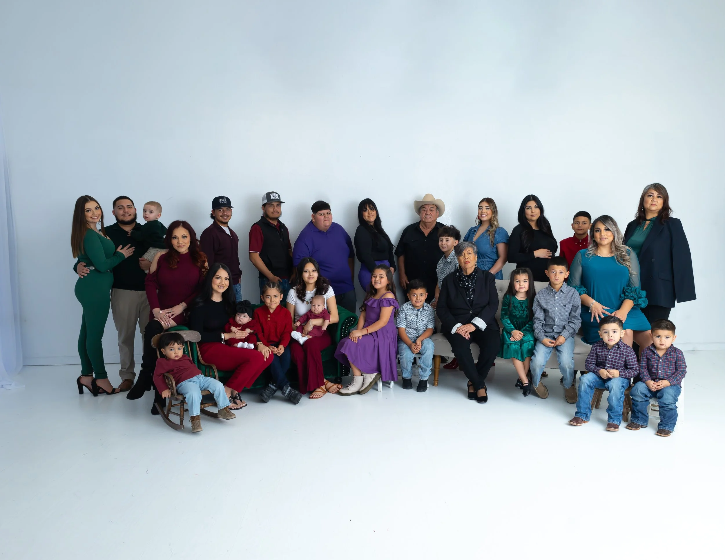 Family group photo with adults and children in colorful clothing, standing and sitting in a studio with a plain white background.