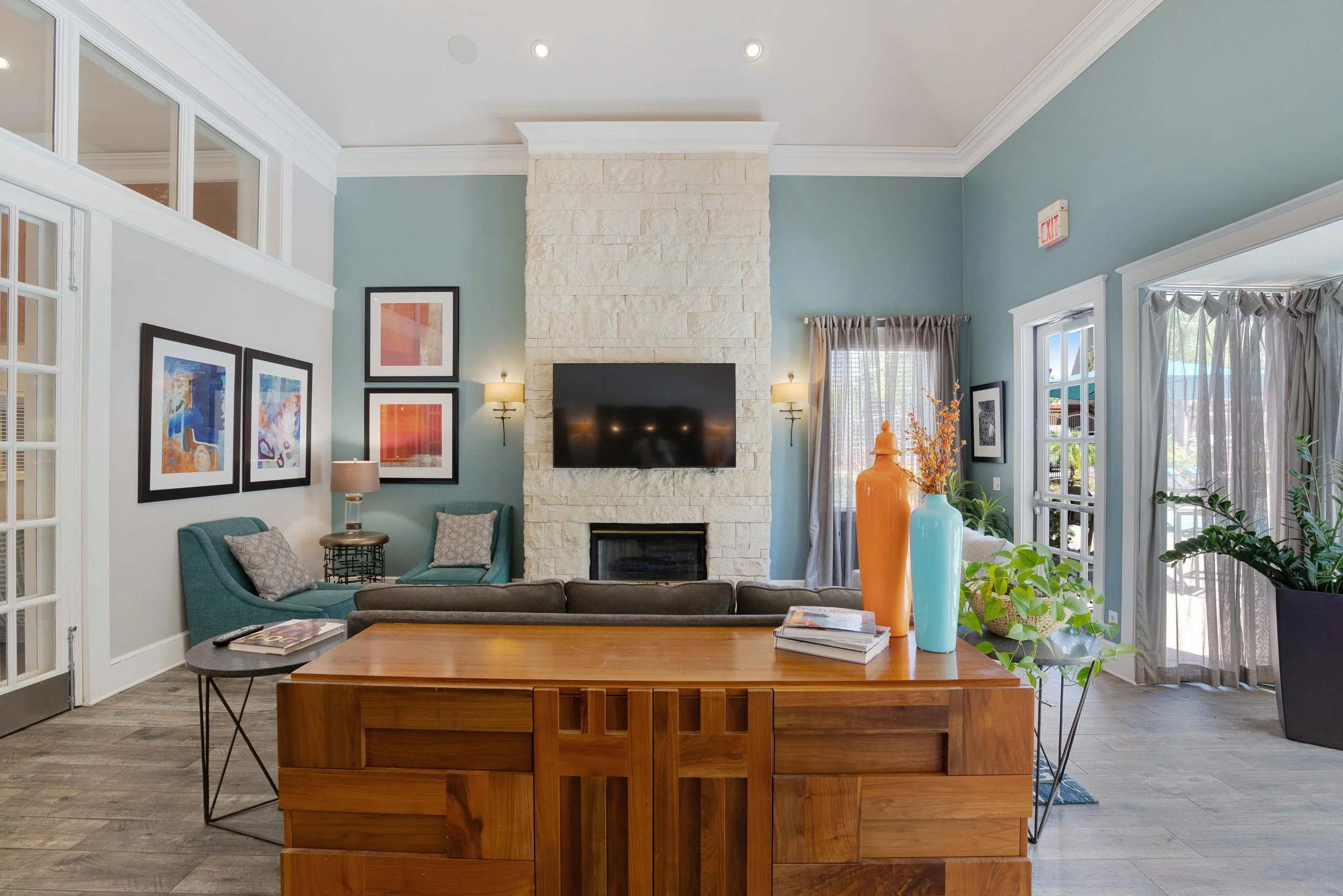 Living room with a stone fireplace, wall-mounted TV, blue accent walls, artwork, and seating, with sliding glass doors leading outside.