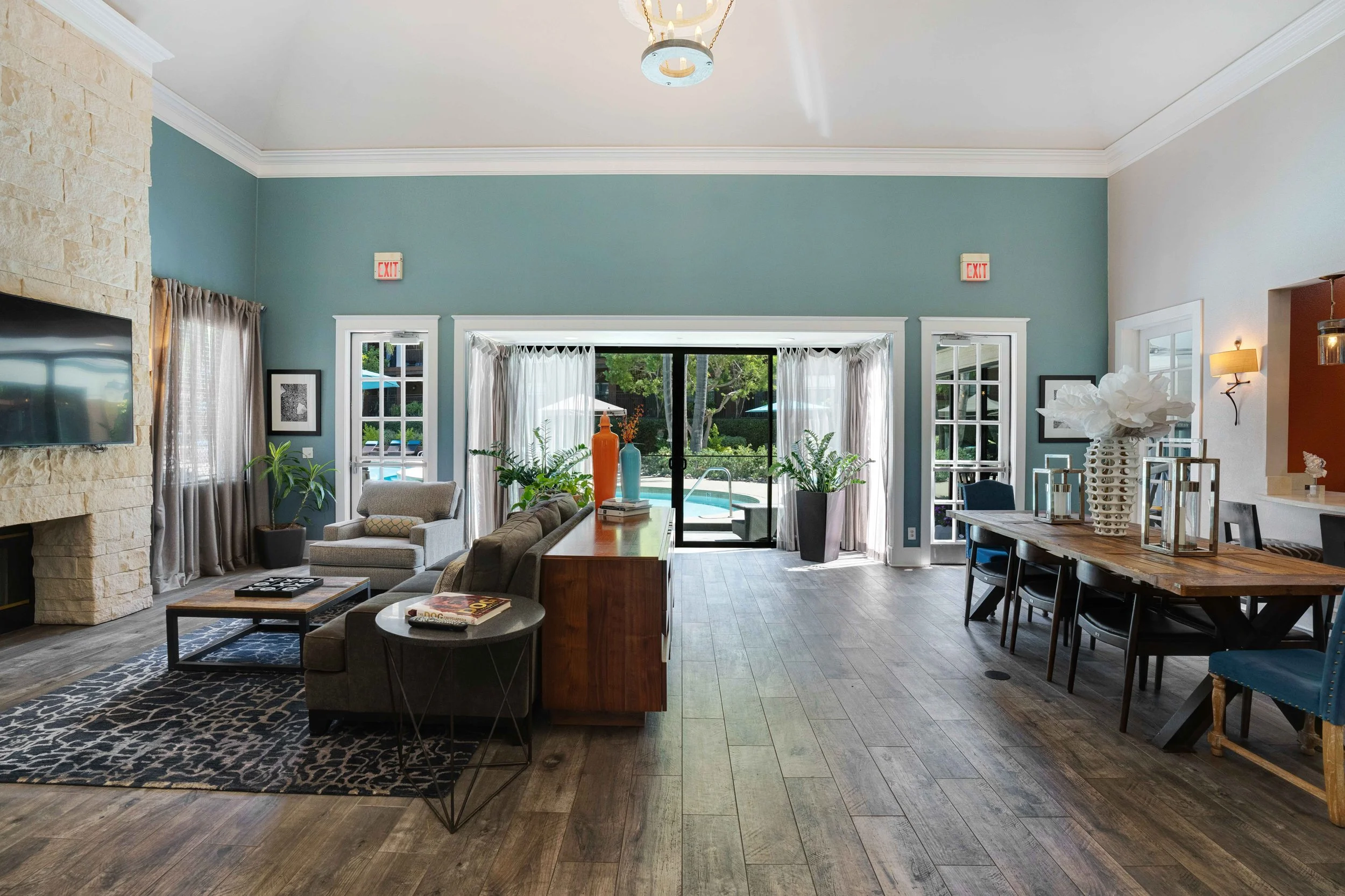 Living room with blue walls, stone fireplace, TV, sofas, coffee table, and sliding glass doors leading to a backyard with a pool.