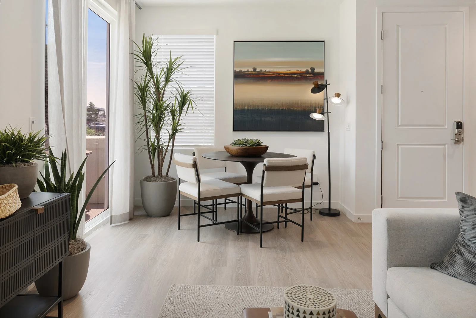 Modern living room with dining area, large potted plants, and a balcony door.