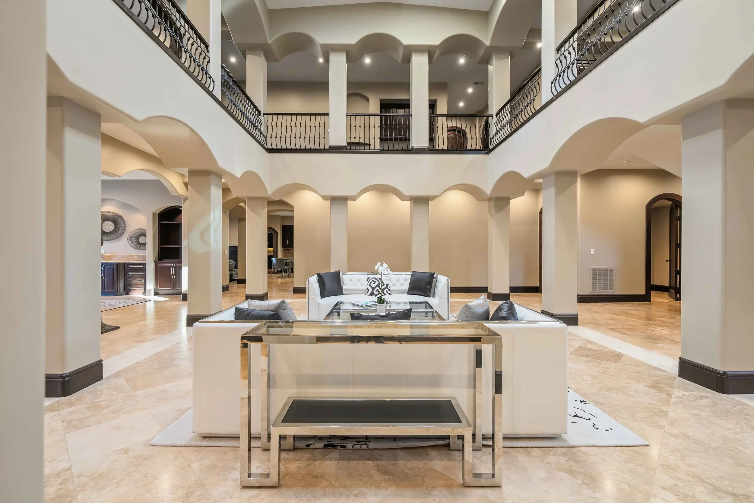 Elegant hotel lobby with marble floors, white sofas with black pillows, a glass-top table, and a modern staircase with black railings leading to the upper level.