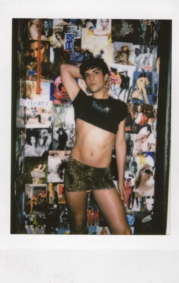Person posing in leopard print shorts and black crop top in front of collage wall.