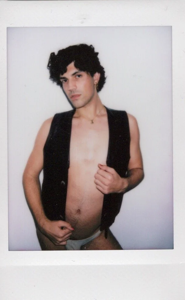 Person posing in a black vest and white underwear with a neutral expression, against a plain background.
