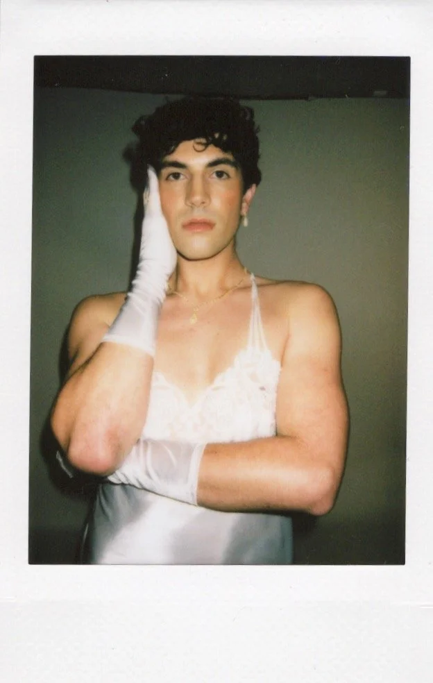 Person in a white lace camisole and gloves posing with hand on face.