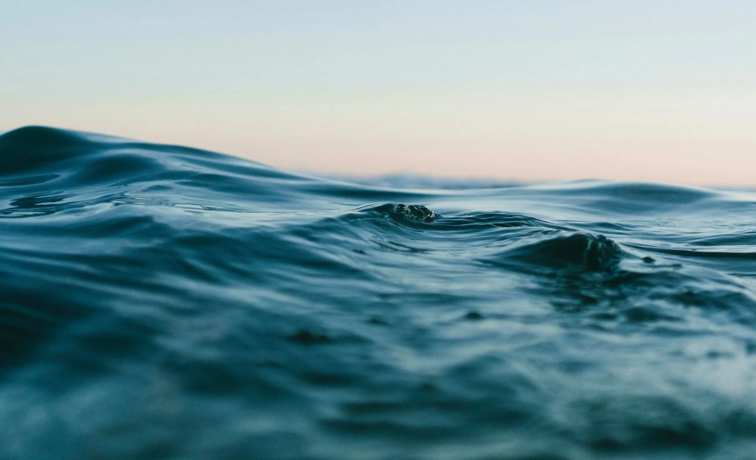Close-up of ocean water with gentle waves and a pastel sky in the background.