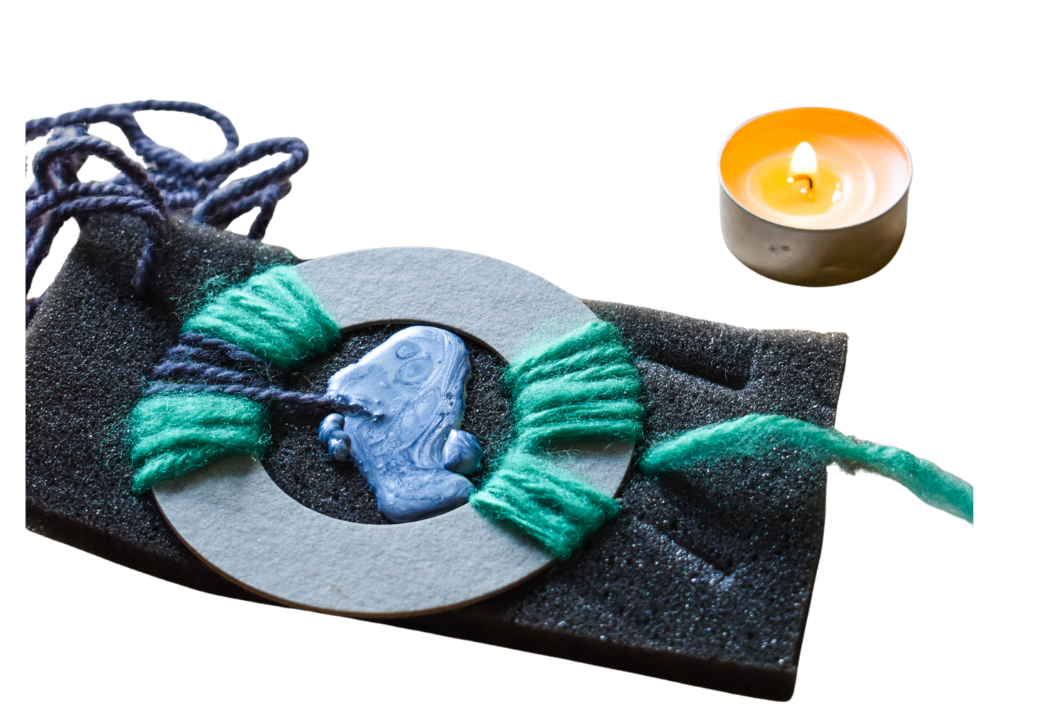 Yarn, sponge, and melted wax artwork placed beside a lit tealight candle.