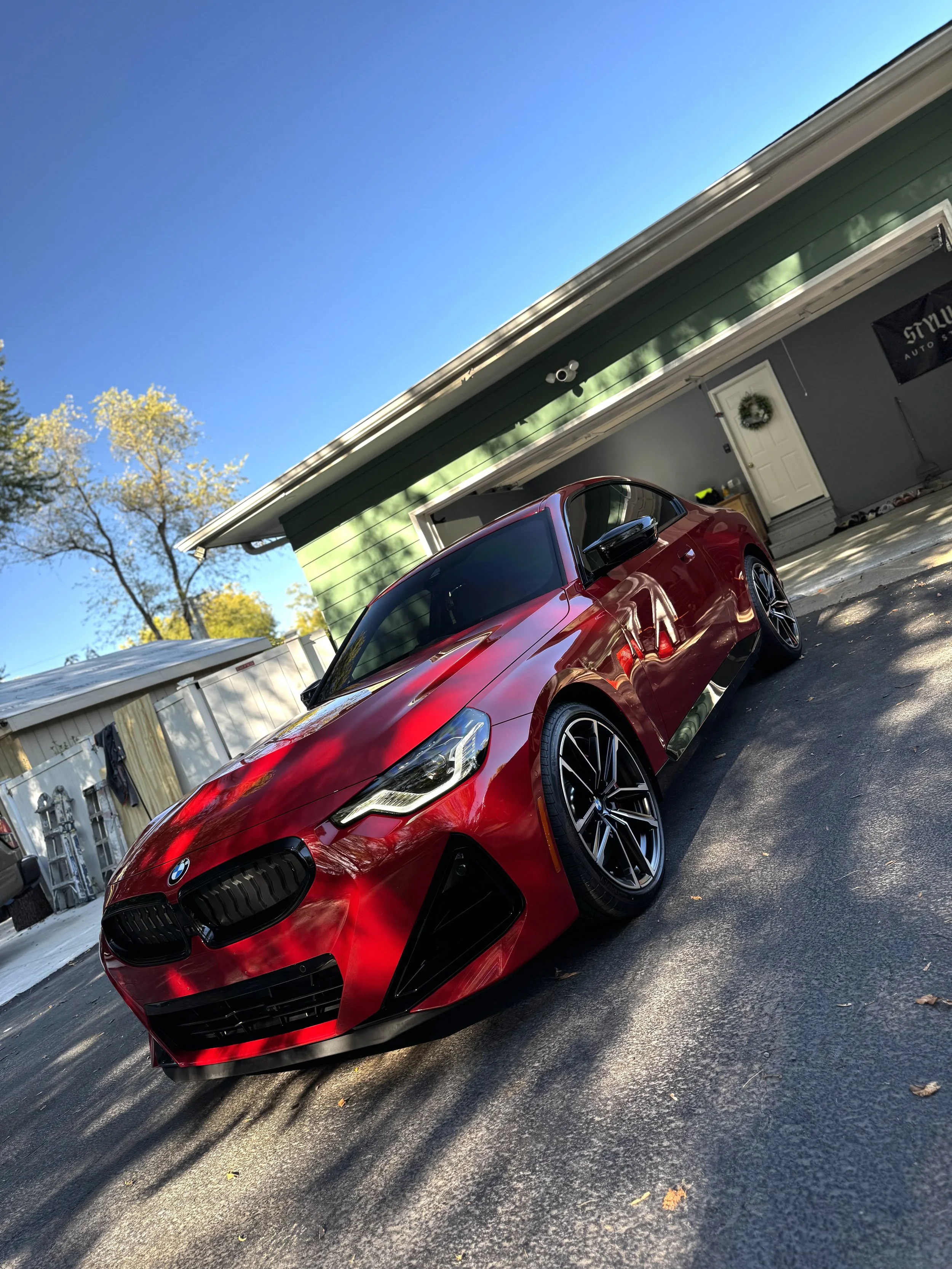Red BMW sports car parked in driveway in front of a green house with a white door.