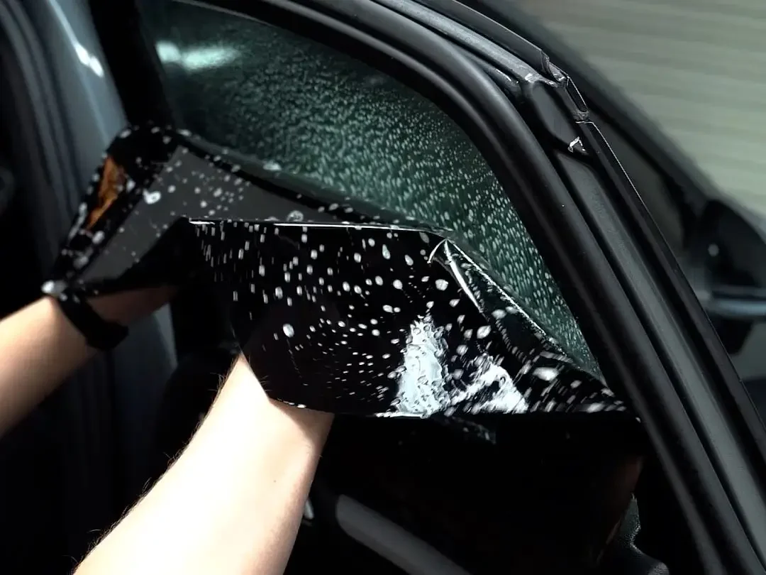 A person cleaning a car's side mirror with a black cloth that has white star-like patterns.