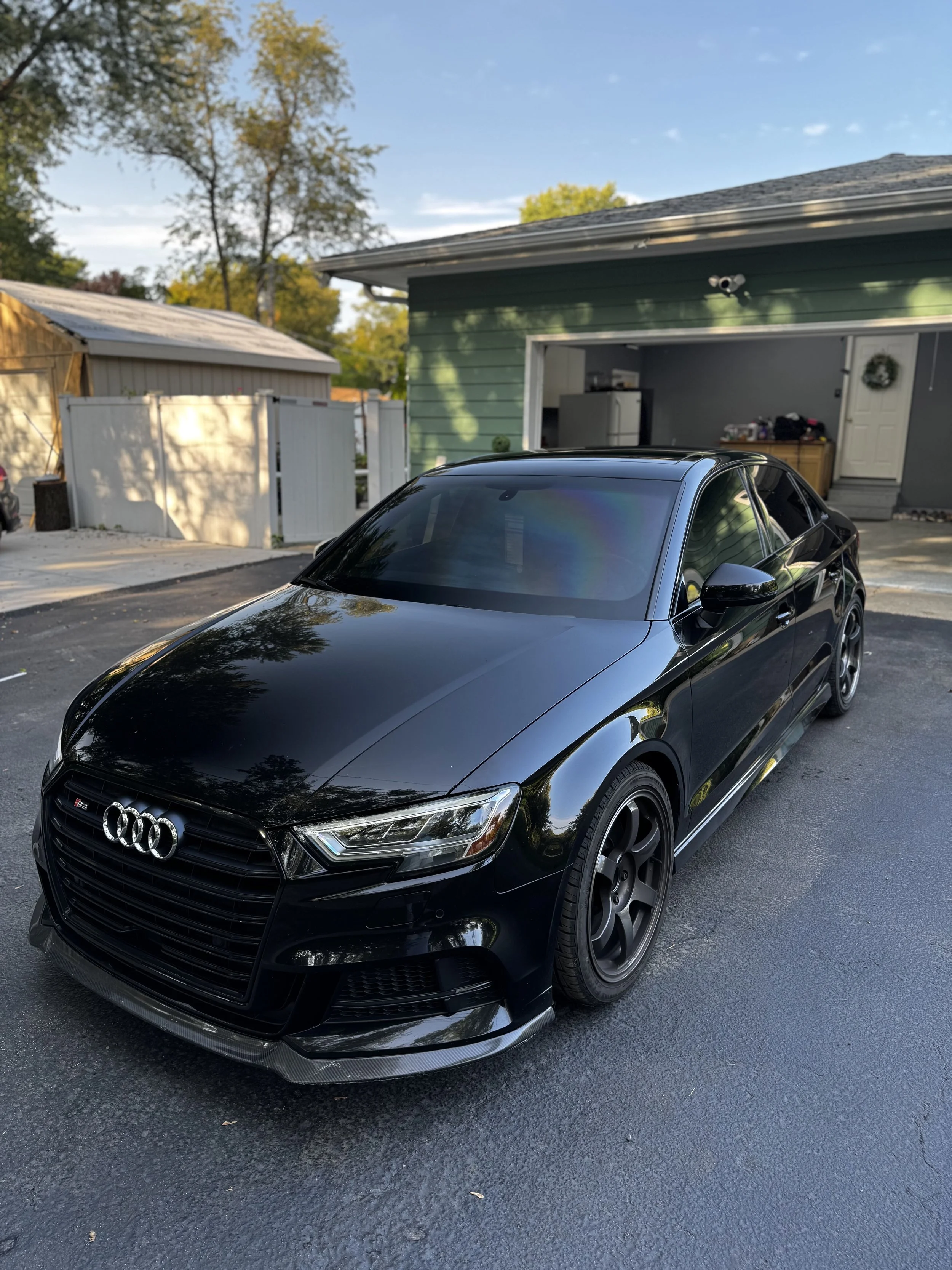 Black Audi sedan parked in a driveway in front of a house with a green exterior and open garage.