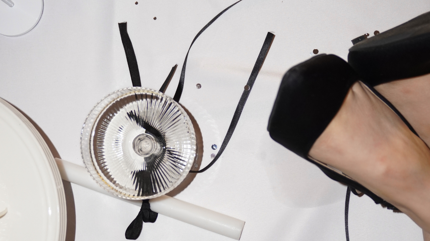 A pair of women's high heel shoes, a glass of water, a white plate, and some black ribbons and confetti on a white surface.