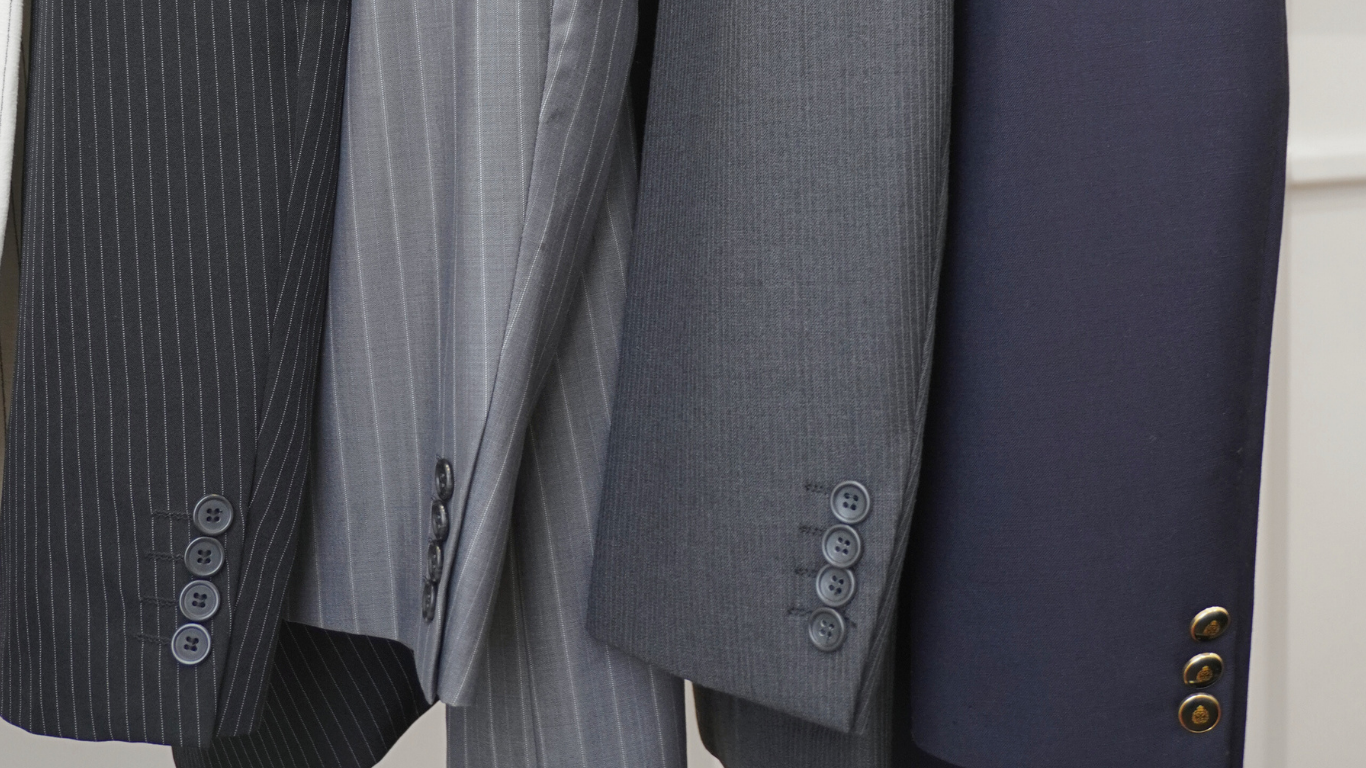 Close-up of suit jackets hanging, showing various patterns and button styles.