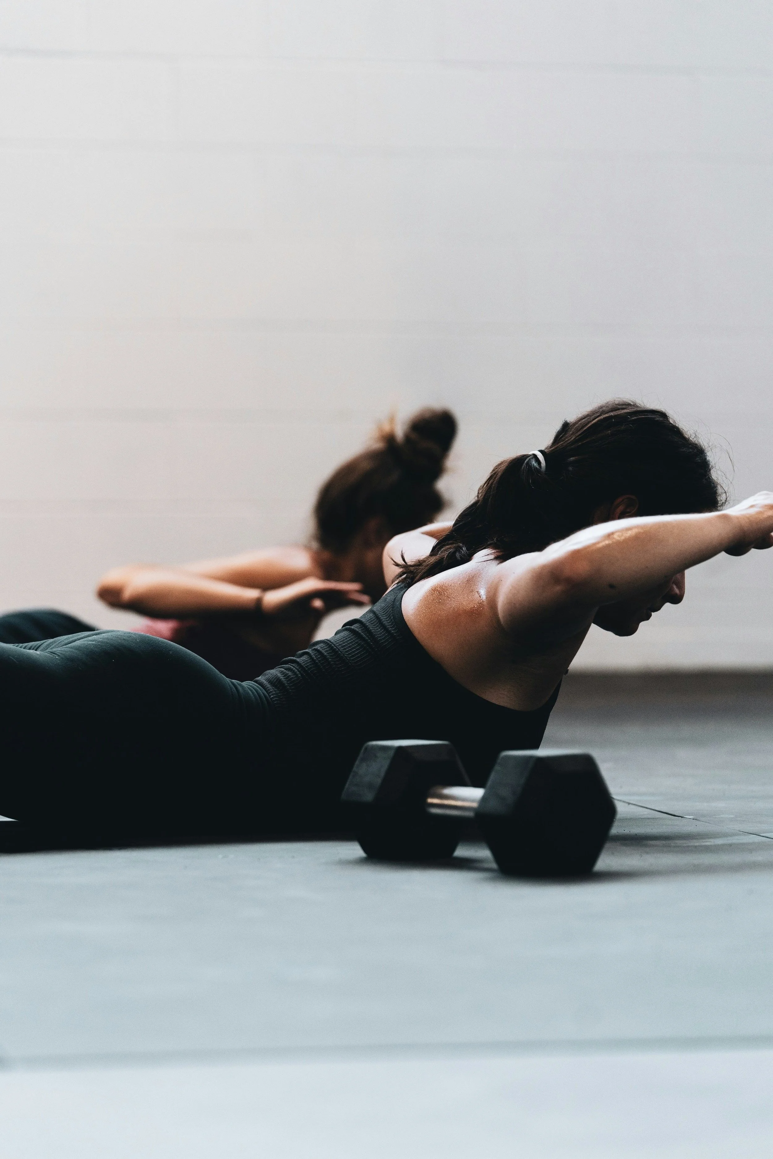 A woman wearing black is in the superman pose with a hand weight next to her
