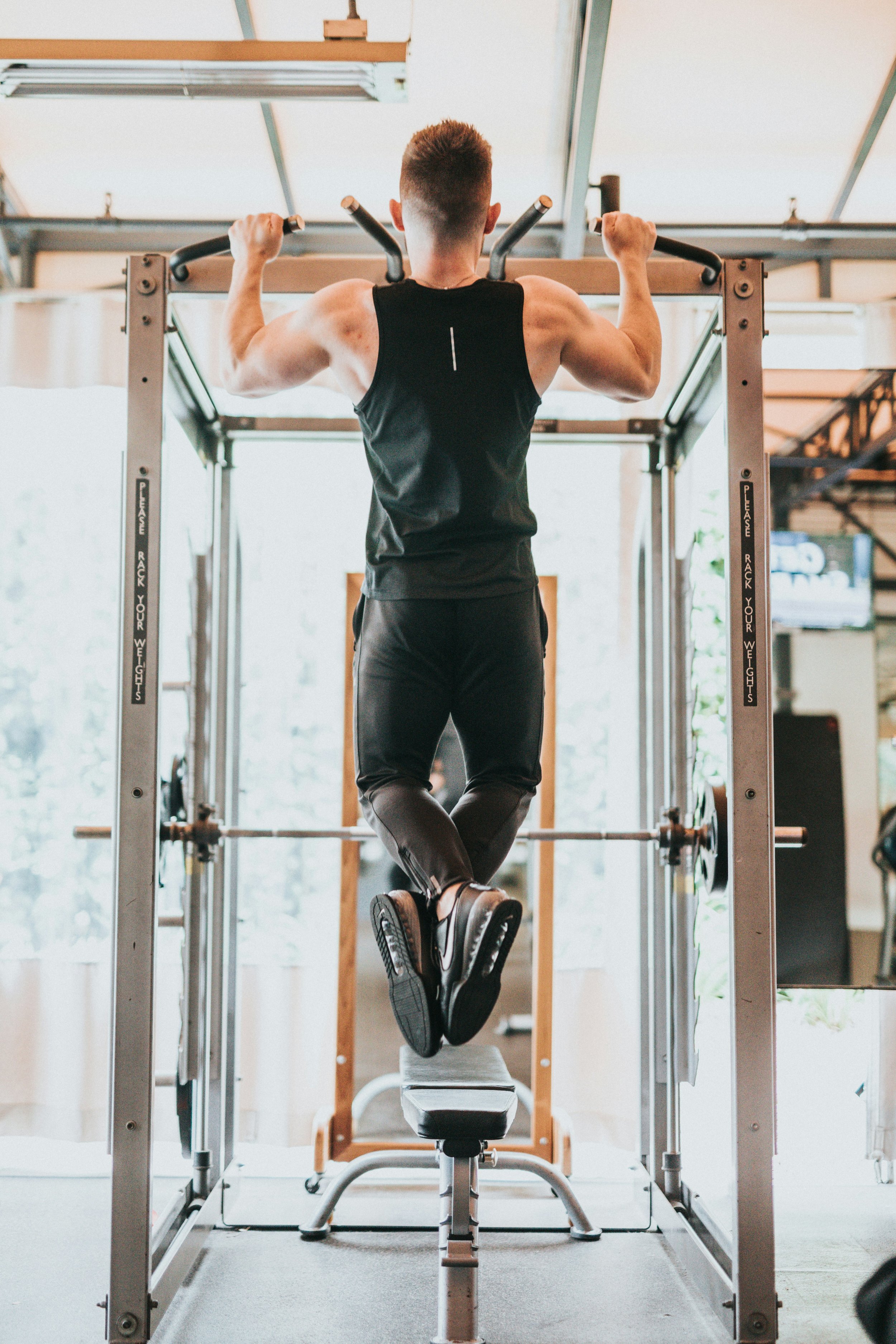 A man wearing all black is doing pull-ups on a machine in the gym