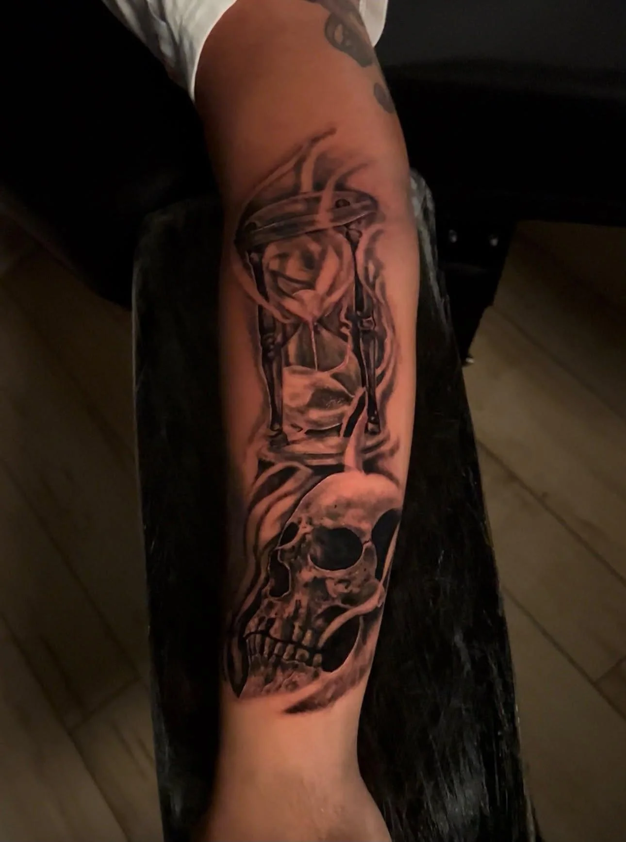 Tattoo of a human skull with flames around it on a person's arm.