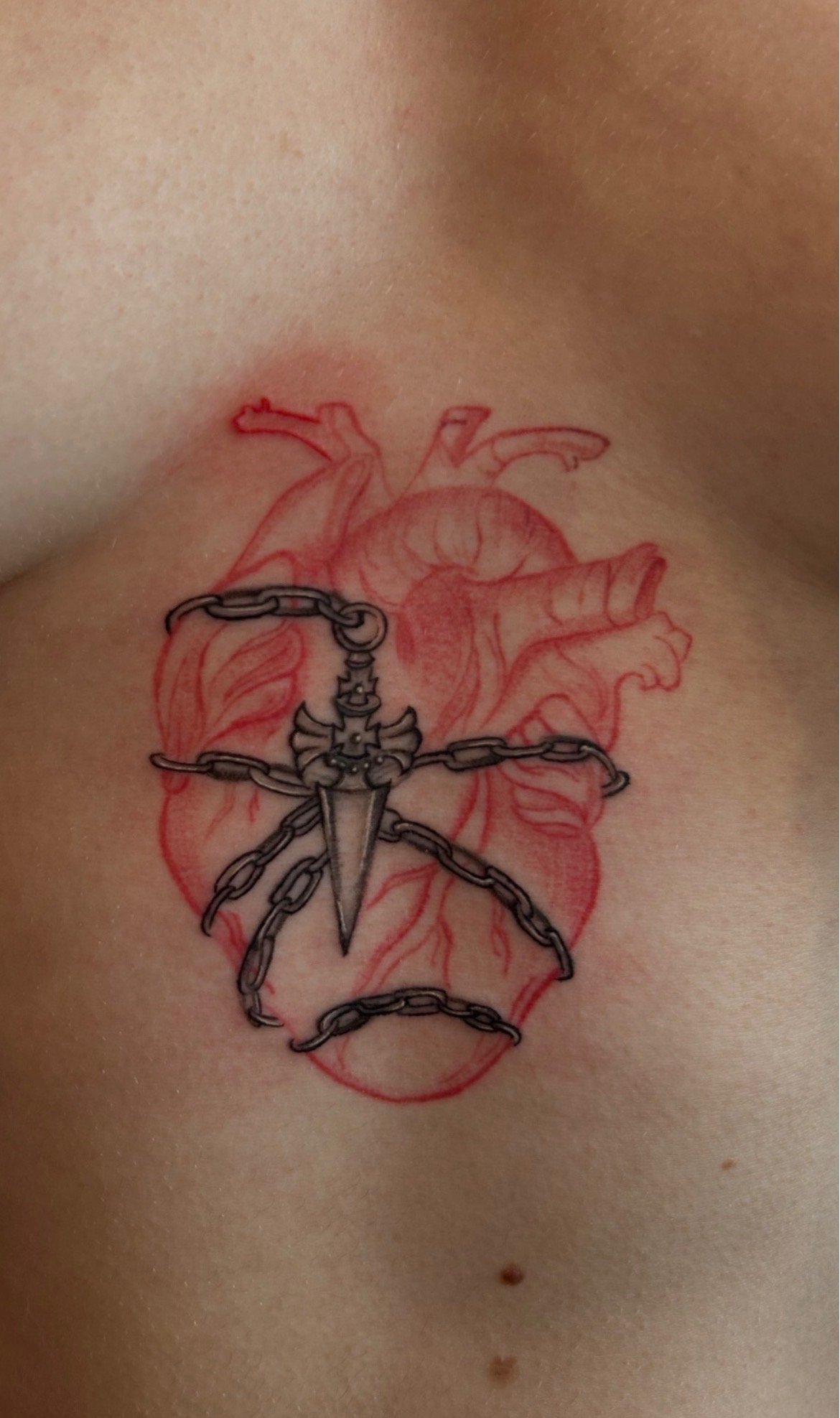 Tattoo of a heart with a sword through it, surrounded by chain links.