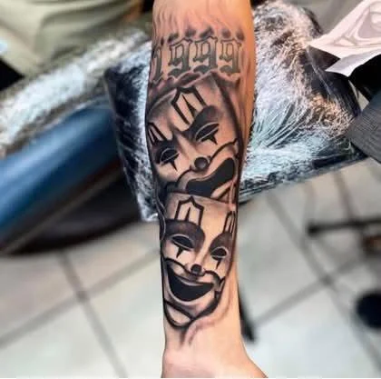 Tattoo of three clown faces on a person's forearm, with stylized black ink artwork.