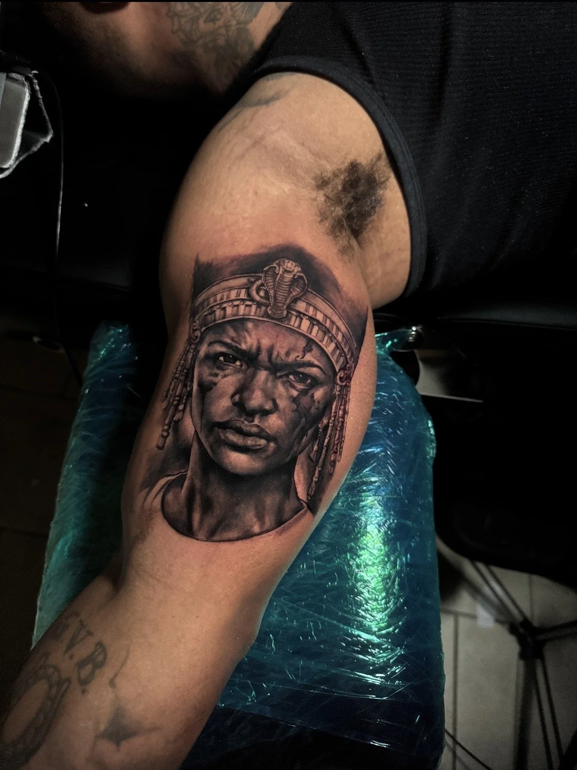 Tattoo of a woman with beads and a headdress on upper arm.