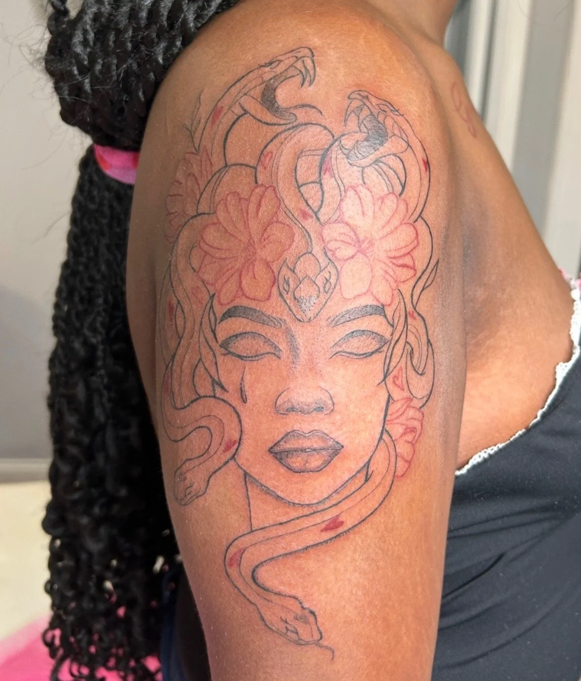 Tattoo of a woman’s face with her eyes closed, surrounded by flowers, and a snake coiled around her head and neck.