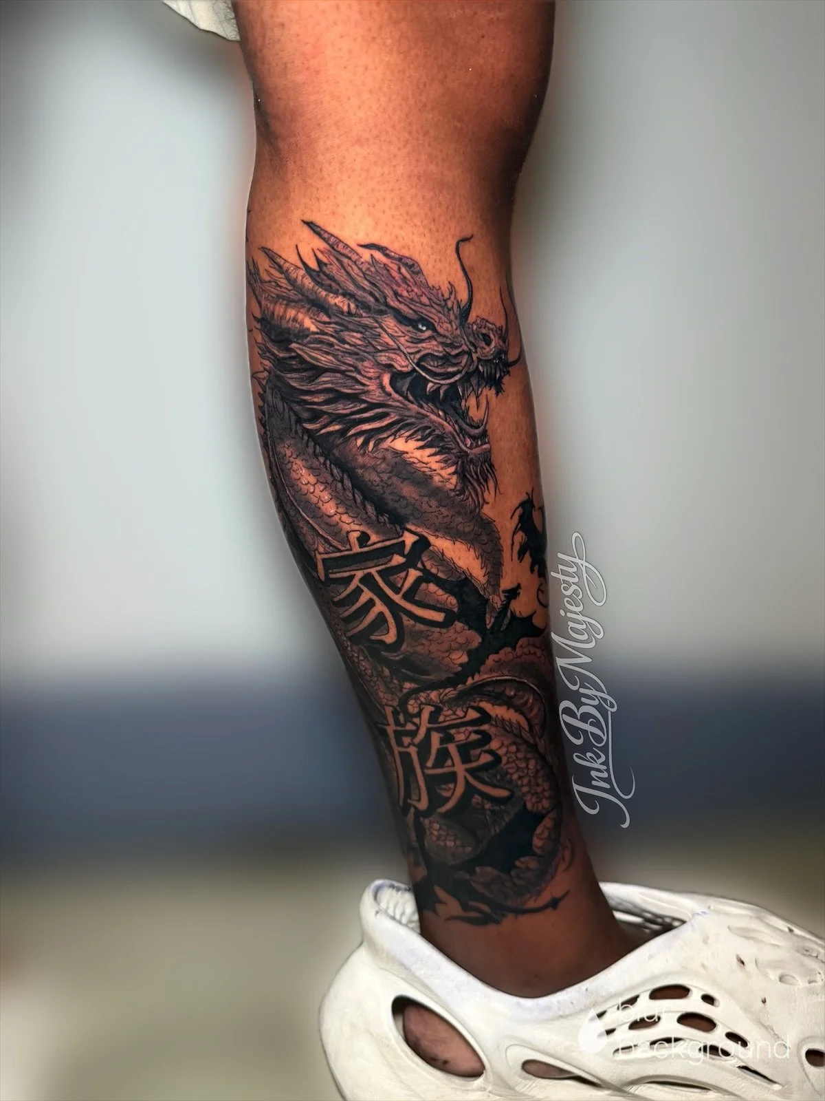 A tattoo of a fierce dragon with detailed scales, sharp claws, and an open mouth, covering most of the person's lower leg and ankle.