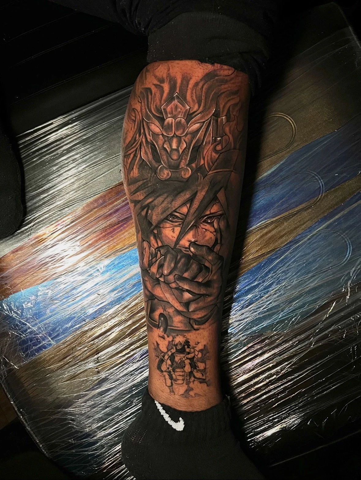 A tattoo sleeve on a person's arm featuring a dragon, a person's face with a lightning bolt, and a warrior in armor wielding a sword.