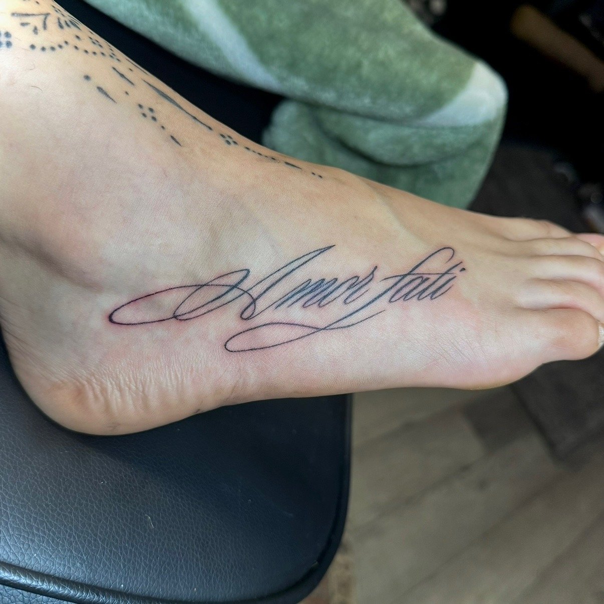 Tattoo of the name 'James Lee' written in elegant cursive script on the top of a person's foot.