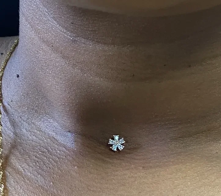 Close-up of a person's neck with a diamond flower-shaped stud piercing.