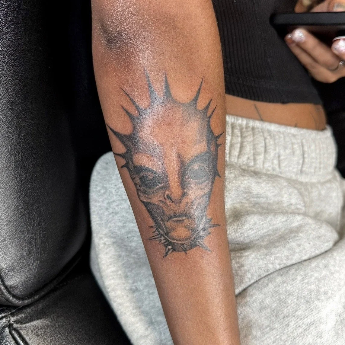 Tattoo of a wolf's face with spiky, sun-like rays around it on person's forearm.