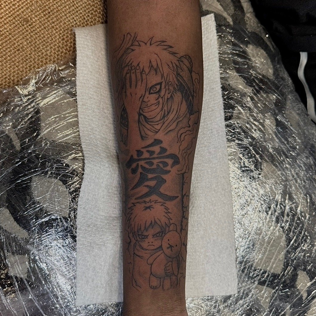 Tattoo on a person's arm featuring characters from an anime, including a smiling character with bright, wild hair and a mischievous expression, a smaller serious character holding a teddy bear, and Japanese kanji characters.