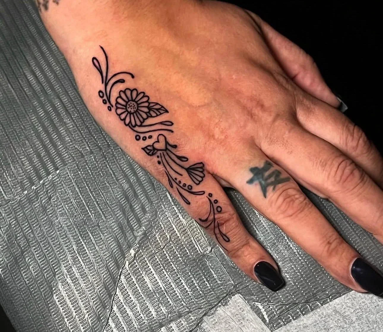 Tattoo of a floral and abstract design on a person's hand, with a small heart and decorative lines.