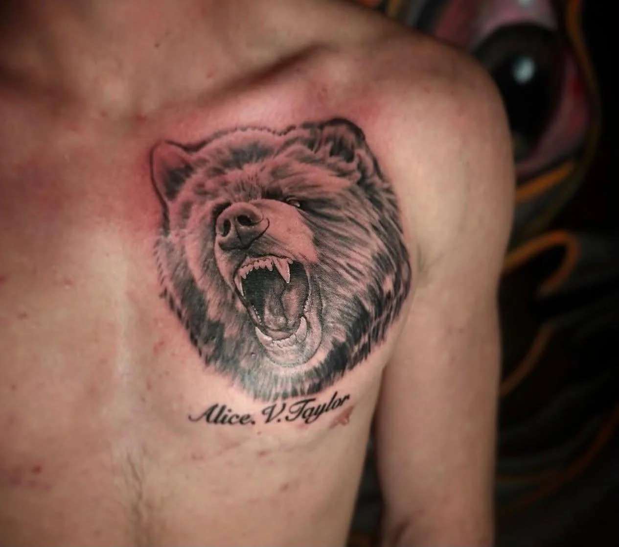 Tattoo of a roaring bear on a person's chest with the name Alice V. Taylor written below.