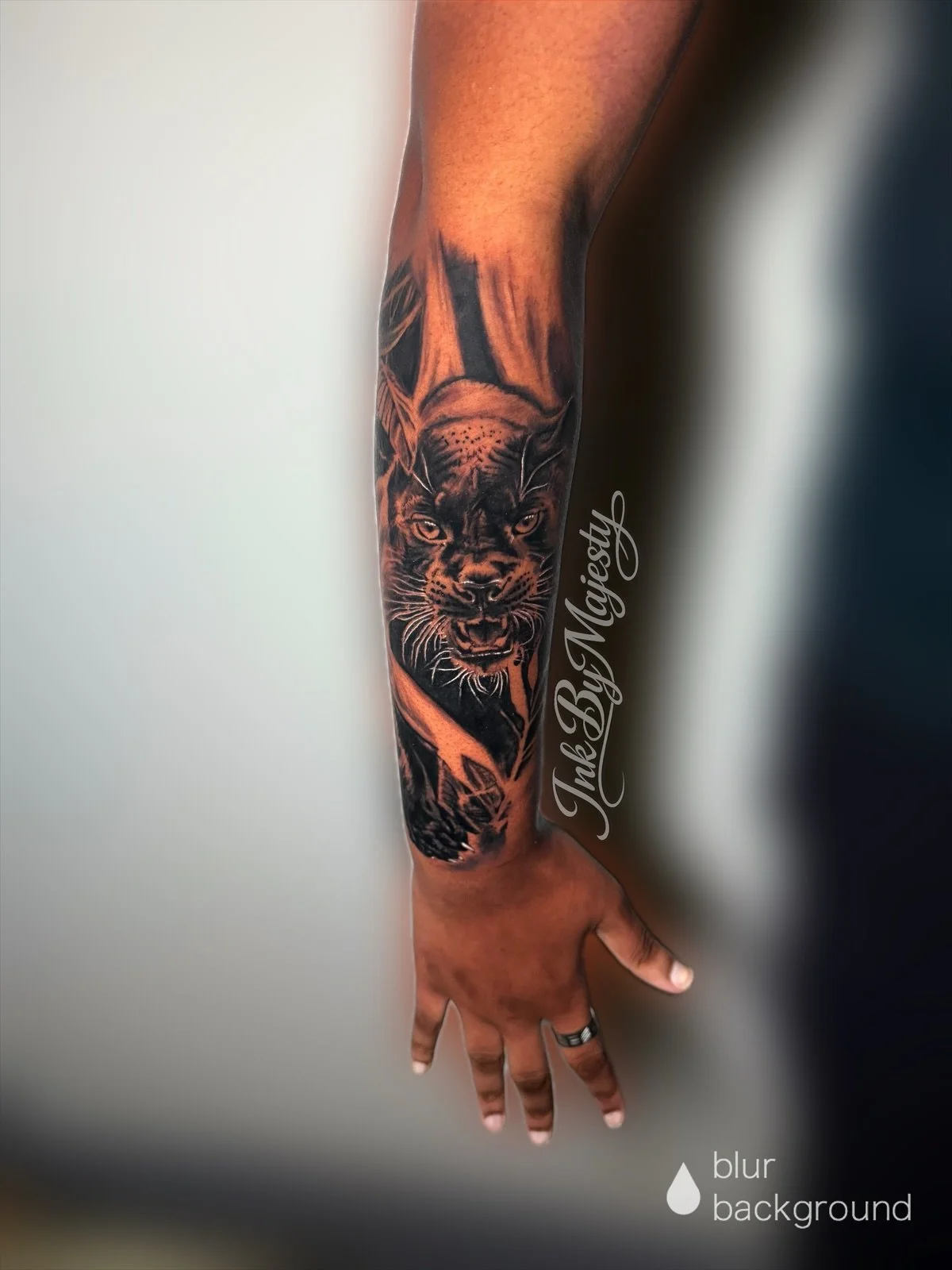 Tattoo of a fierce-looking black panther with piercing eyes on a person's forearm, with a phrase in cursive script along the side and a blur background.