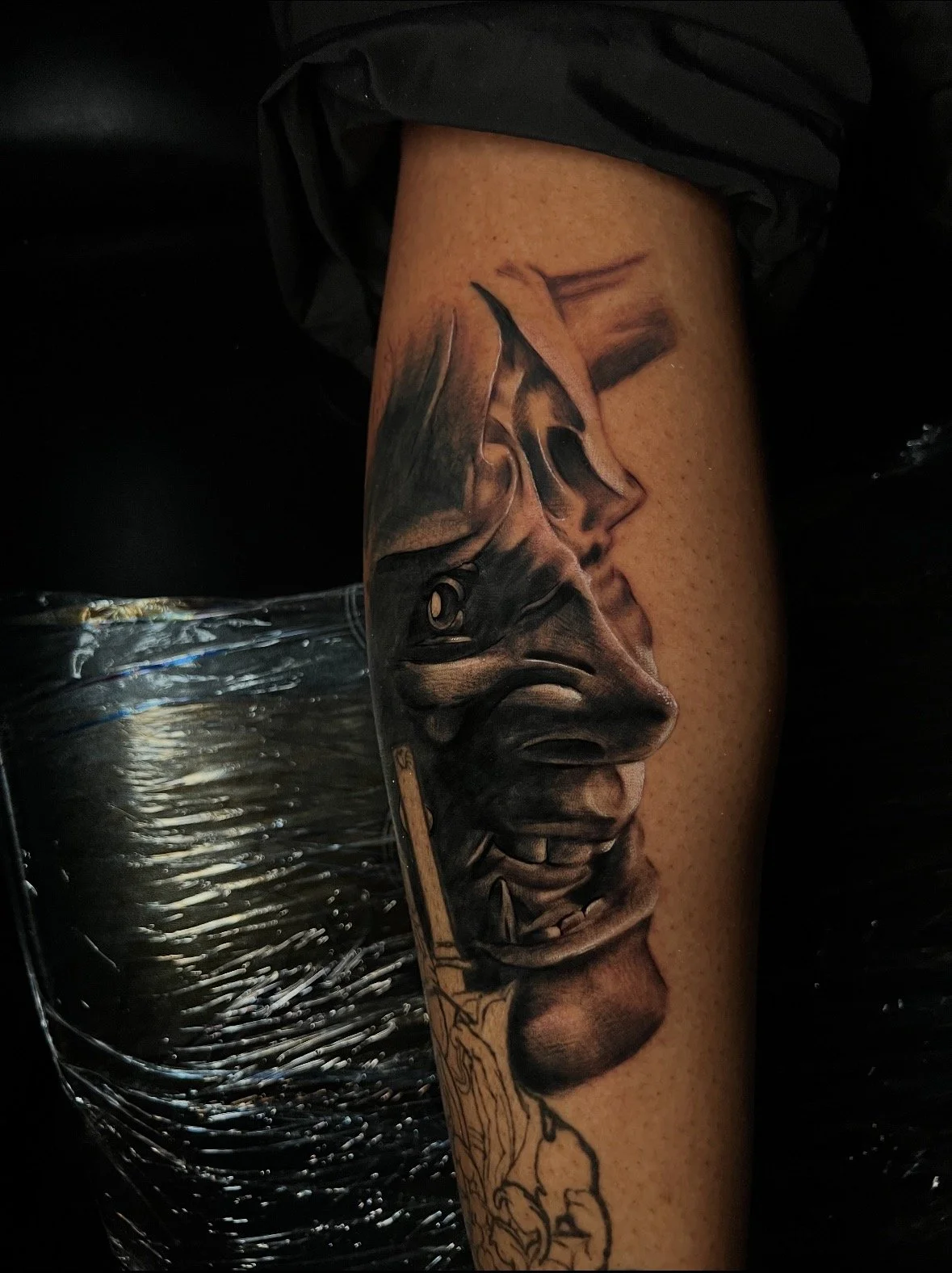 A black and gray tattoo of a human face with sunglasses and tears, on a person's forearm.