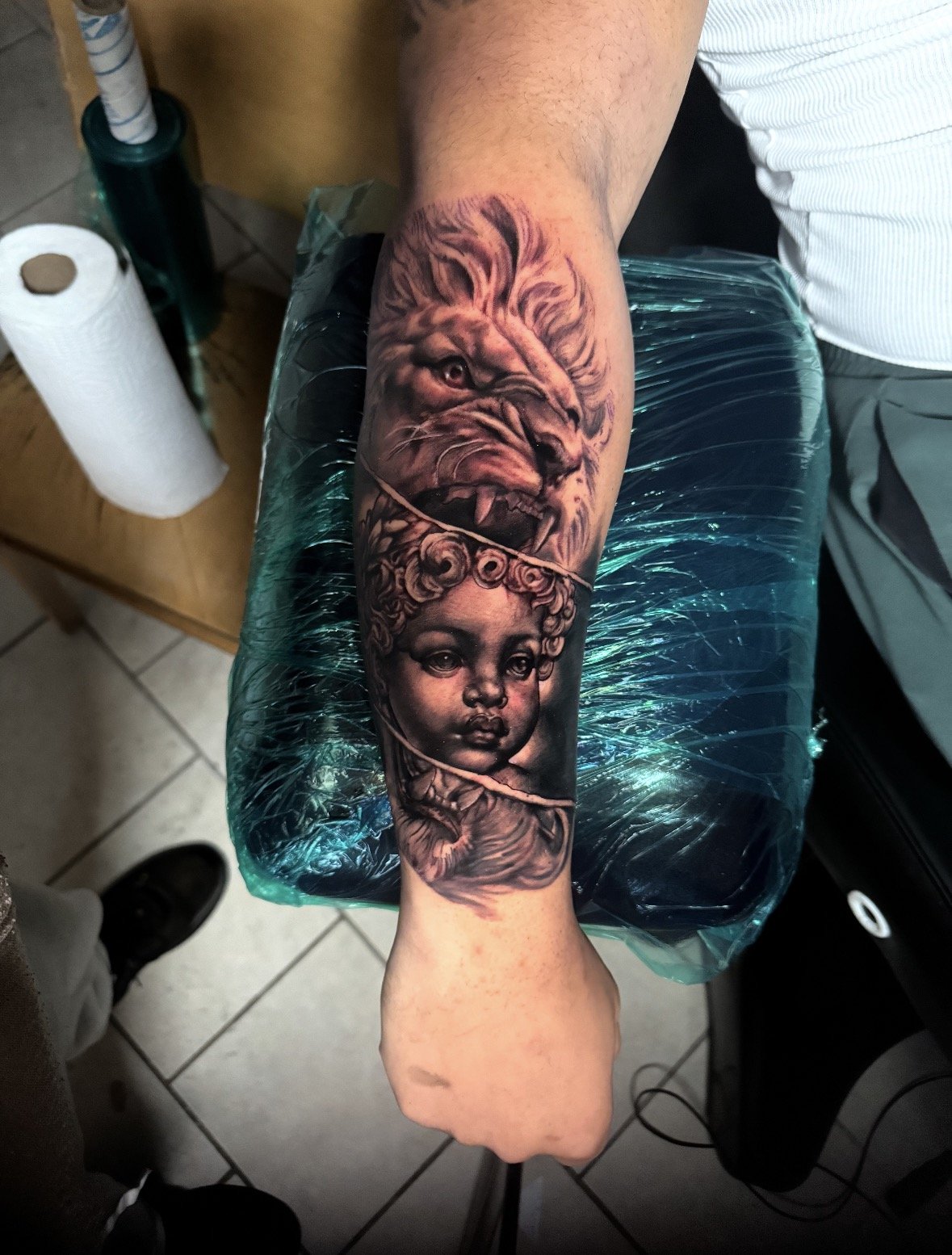 A tattoo sleeve featuring a lion's head and a child's face on a person's forearm.