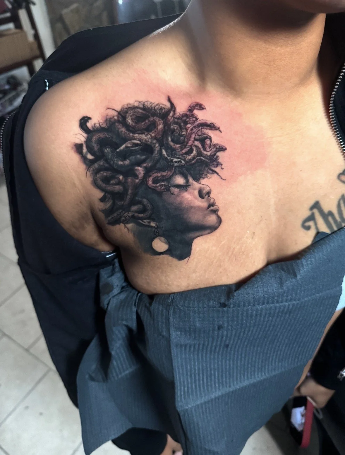 Tattoo of a woman's side profile with curly hair, wearing a large earring, on person's chest.