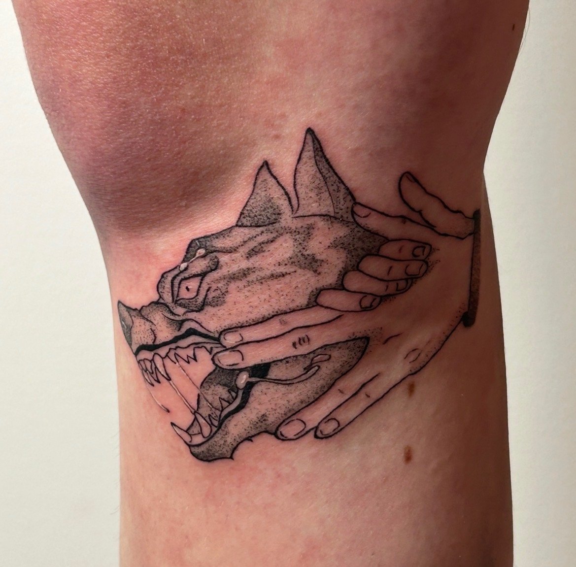 Black outline tattoo of a dog's head being held by two hands.