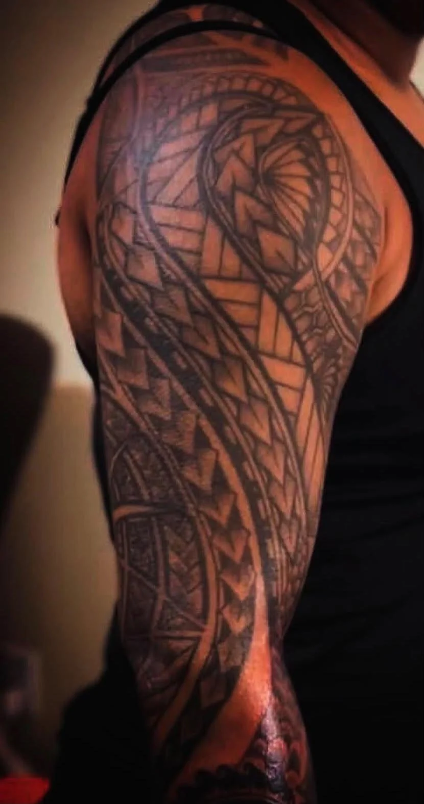A person's upper arm with an intricate geometric tribal style tattoo that covers the shoulder and extends down the arm.