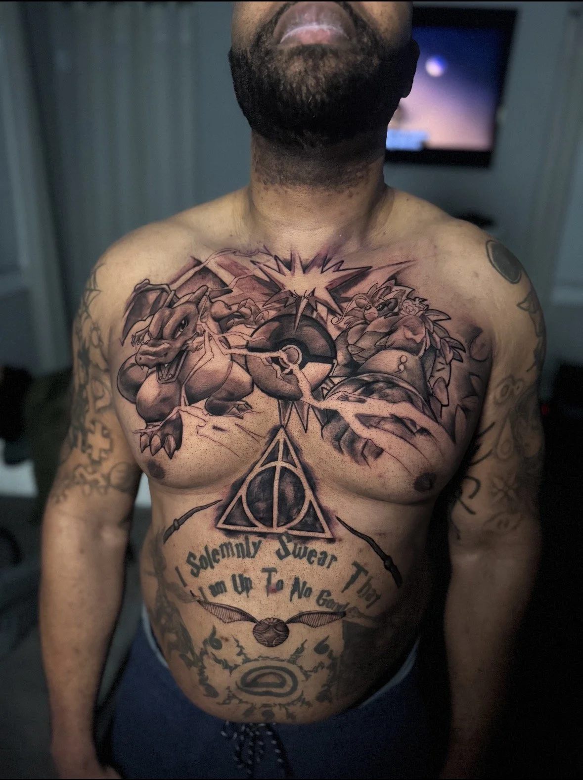 A man with multiple tattoos on his chest, including a cartoonish Charizard Pokemon, a Pokéball, and a Harry Potter Deathly Hallows symbol with the words "Solemnly Swear That I am Up To No Good".