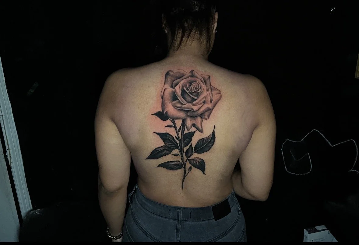 A person's back with a large, detailed black and gray tattoo of a rose.