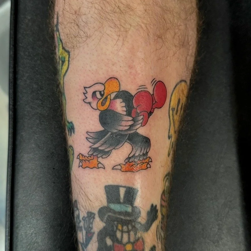Tattoo of a cartoon turkey with boxing gloves on its wings, standing on two feet.