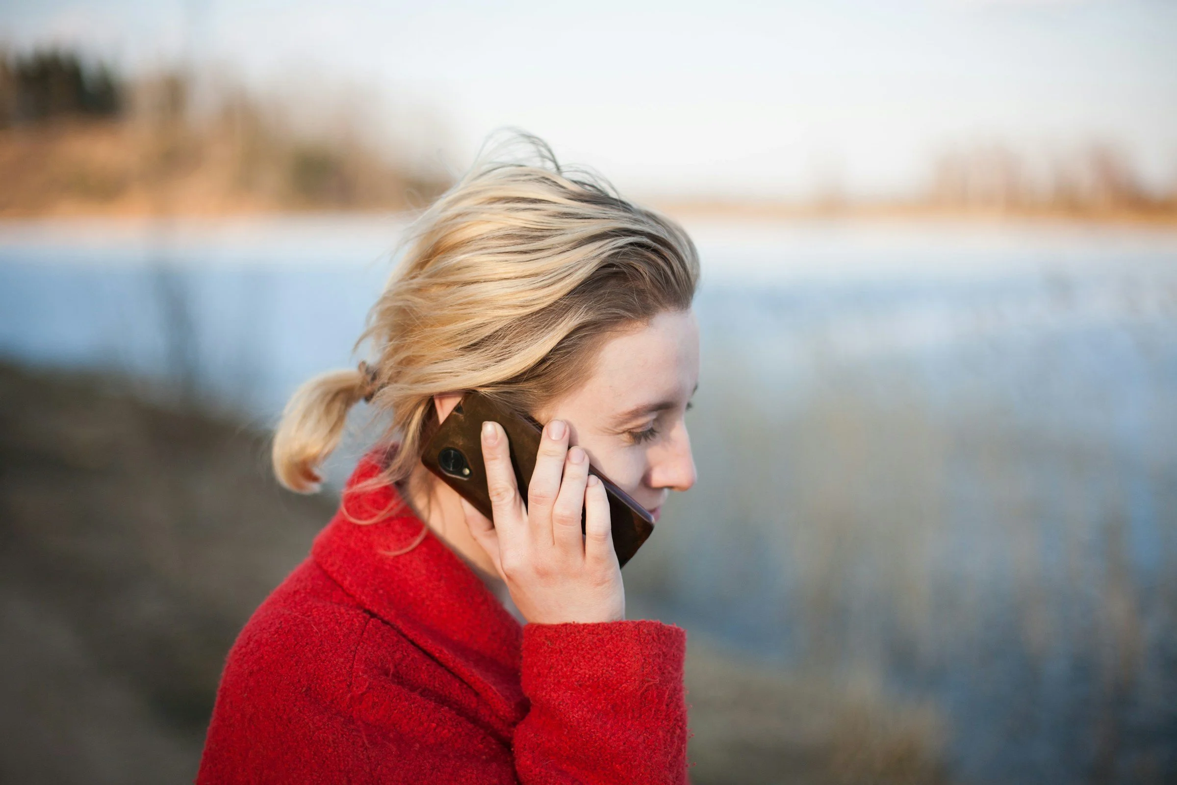 Person in a red coat talking on a phone outdoors near water