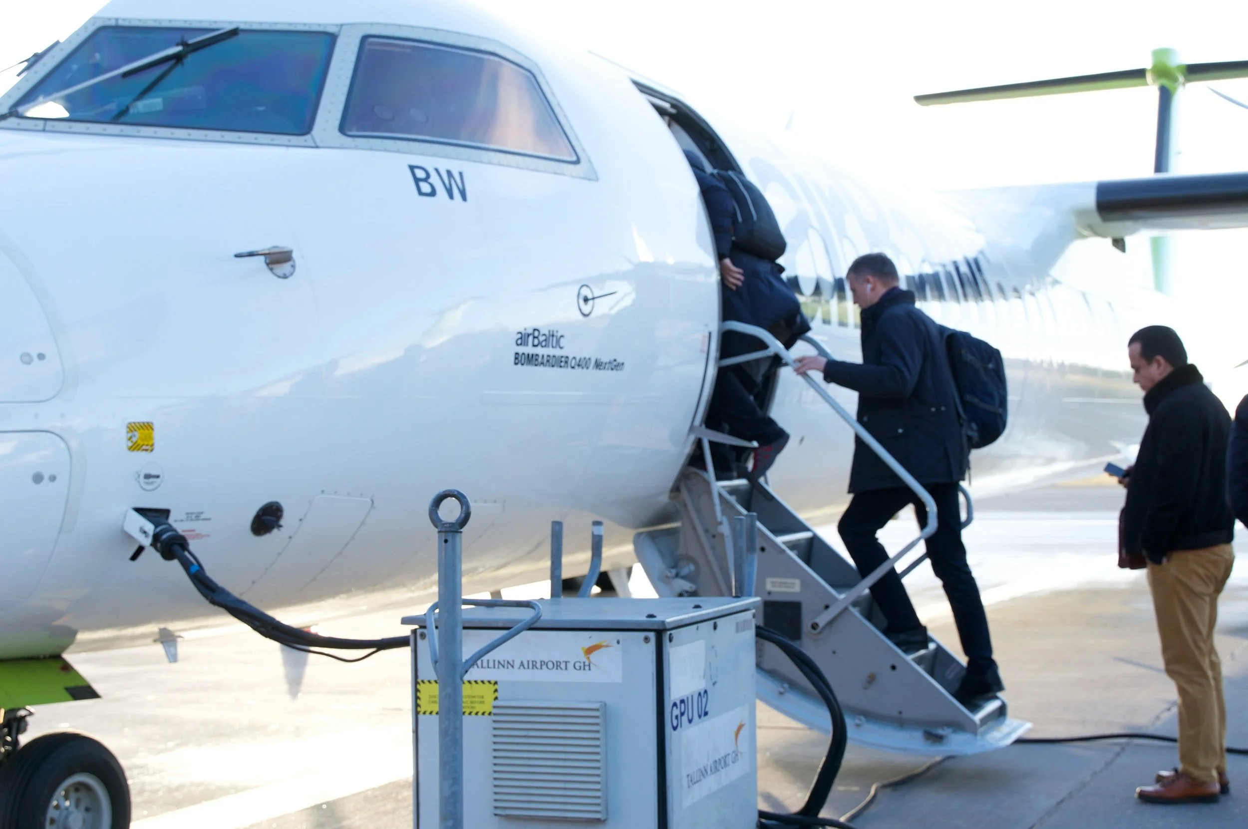 Passengers boarding an airBaltic Bombardier Q400 airplane via mobile stairs at an airport.