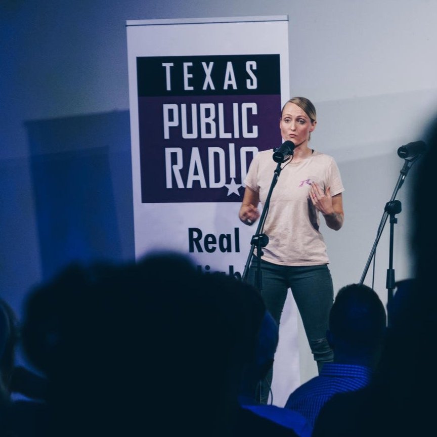 A woman motivational and inpirational speaking into a microphone on stage with Texas Public Radio signage in the background.